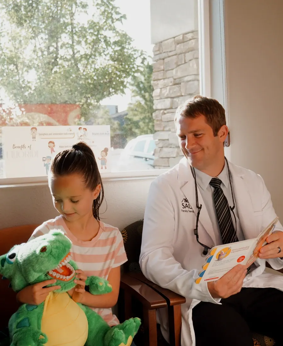 Dr. Jeff reading with a young patient holding a toy dinosaur.