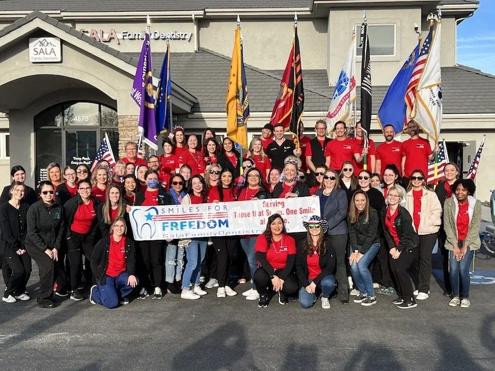 Volunteers, veterans and the Sala team with a Smiles for FREEdom banner outside the practice.